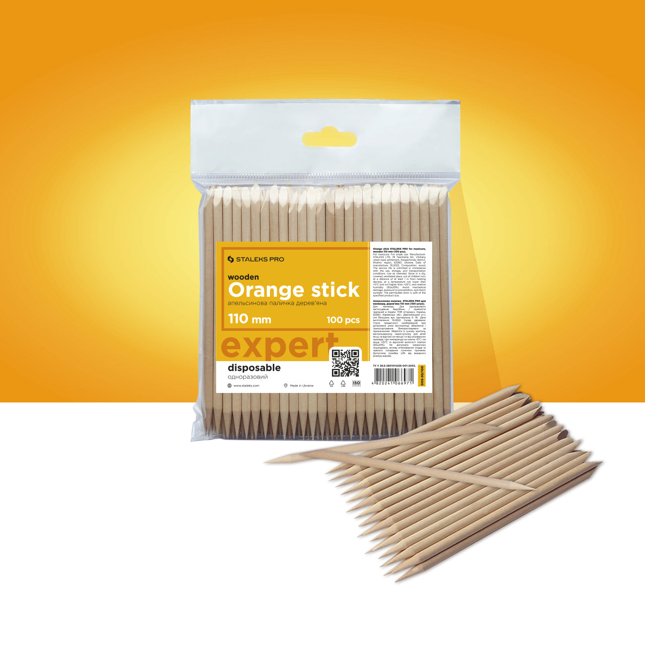 A pack of STALEKS PRO Orange sticks for manicure wooden 110 mm (100 pcs), labeled as "wooden manicure sticks," displayed against a vibrant orange background with some sticks scattered in front.