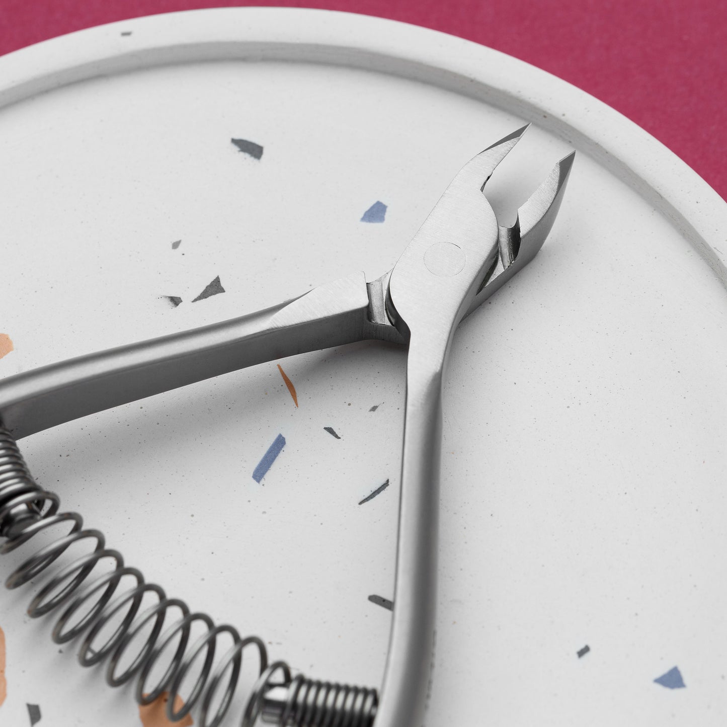 Close-up of a rust-resistant stainless steel STALEKS PRO Professional cuticle nippers with a spiral spring, lying on a white plate with speckled details against a pink background.