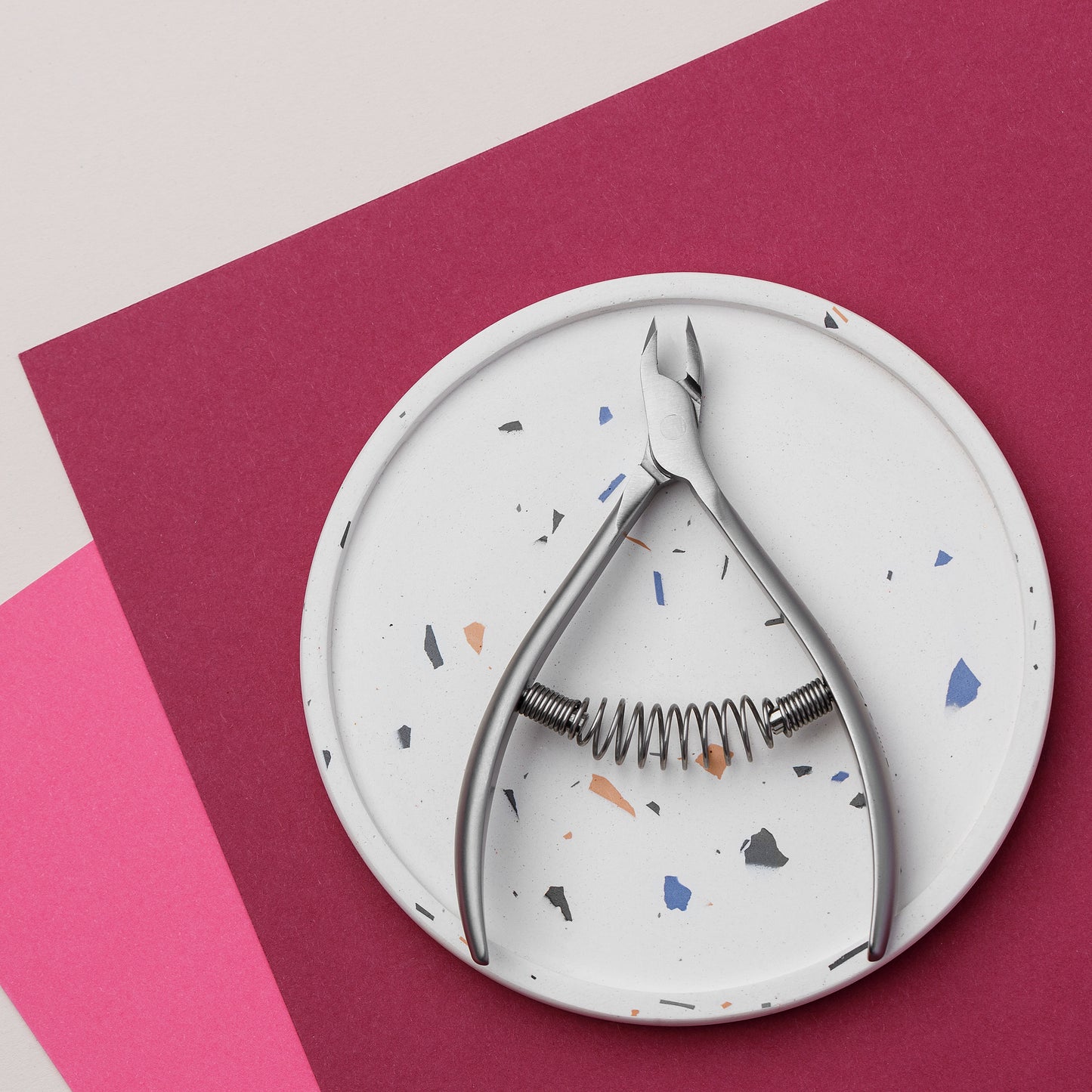 A Staleks nutcracker placed on a circular terrazzo plate, set against a dual background of pink and white. The scene is brightly lit and features geometric simplicity. The nutcracker is made of rust.