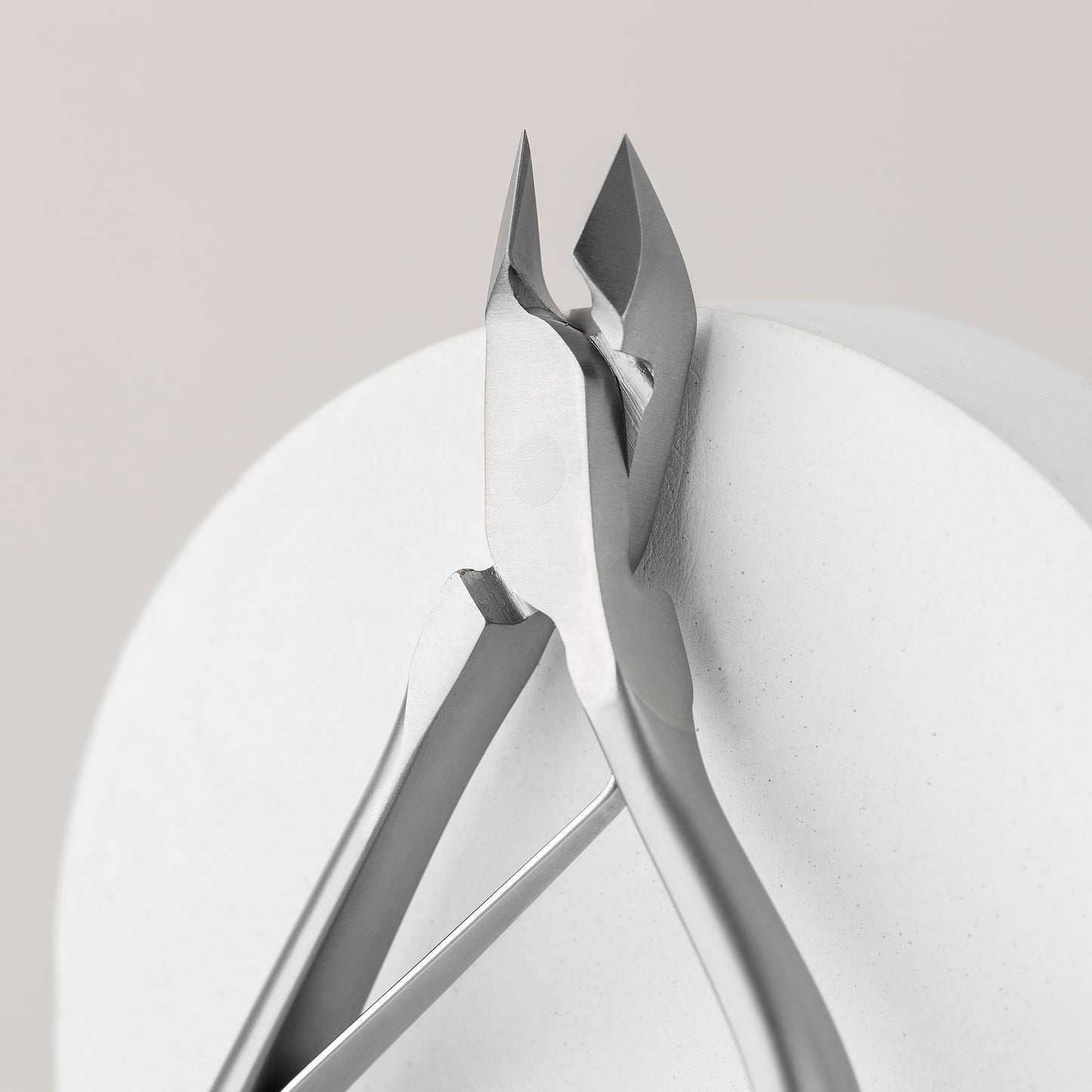 A close-up of the STALEKS PRO Professional cuticle nippers SMART 80 7 mm by Staleks, showcasing their sleek, modern design on a smooth, white circular surface. The focus is on the precision and sharpness of the cutting blades—perfect for a professional manicure or pedicure. The background remains simple and neutral.