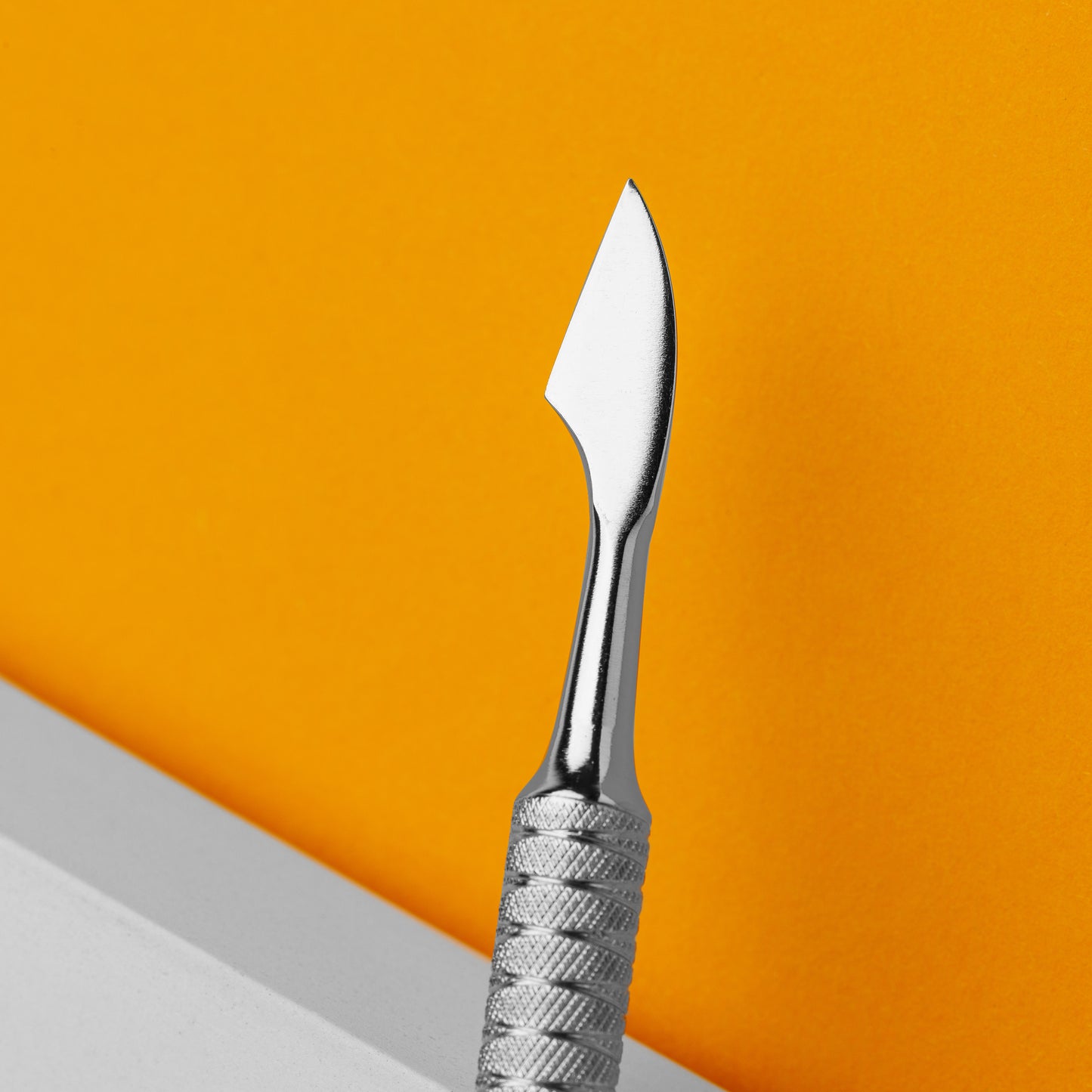 Close-up of a STALEKS precision craft knife with a sharp AISI 420 stainless steel blade and textured metal handle, set against a vibrant orange background.