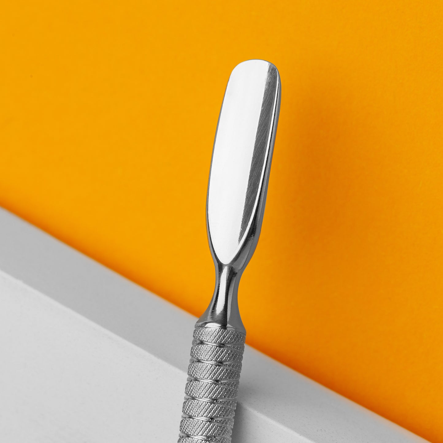 A Staleks STALEKS PRO Manicure pusher EXPERT 30 TYPE 3 (rounded wide pusher and cleaner) made of AISI 420 stainless steel, with a textured handle, standing vertically against a white and orange background.