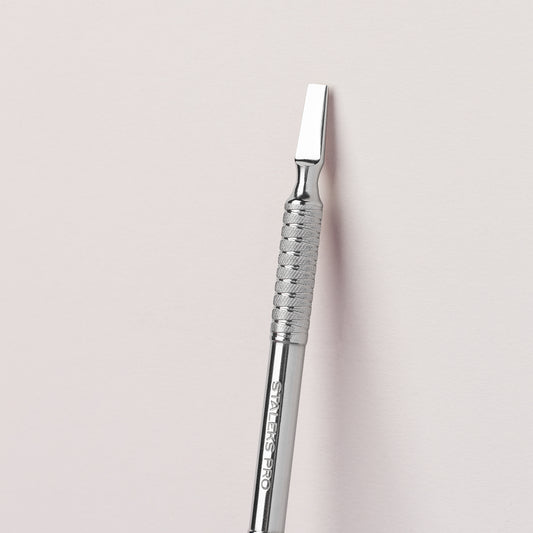 A STALEKS PRO Manicure pusher EXPERT 30 TYPE 5 with a textured grip lying on a soft pink background, detailed with the brand "Staleks" etched into the handle, ideal for both manicure and pedicure.