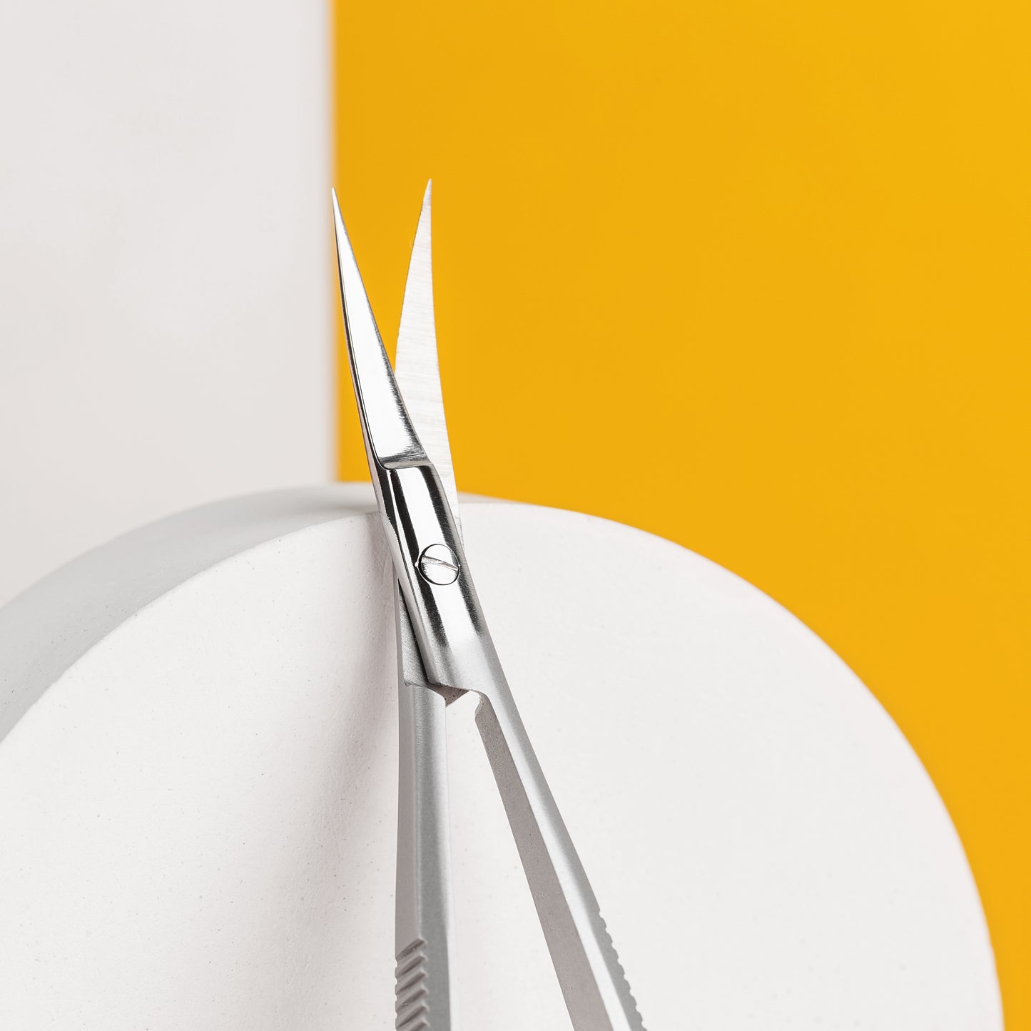 A pair of Staleks EXPERT 90 TYPE 1 Professional micro scissors with open blades positioned on the edge of a white plate against a dual background of white and yellow, allowing a clear overview of the cut line.