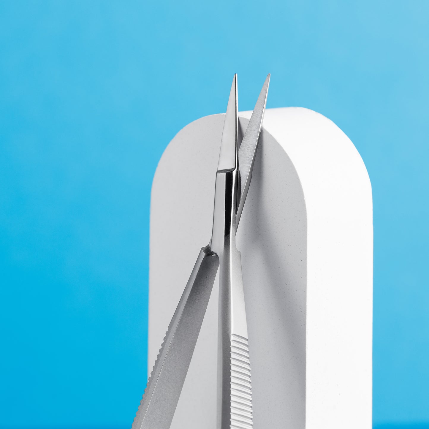 A pair of Staleks PRO Professional micro scissors for eyebrows modeling EXPERT 90 TYPE 2 made from AISI 420 stainless steel with sharp, aligned tips, prominently displayed against a blue background, resting on a white curved surface.
