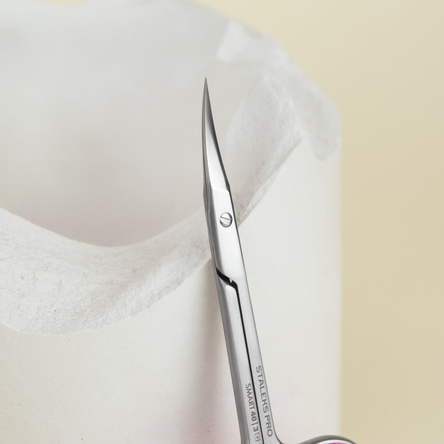 Close-up of ergonomic Staleks stainless steel surgical scissors emerging from a sterile paper wrapping, indicating preparation for a medical procedure.