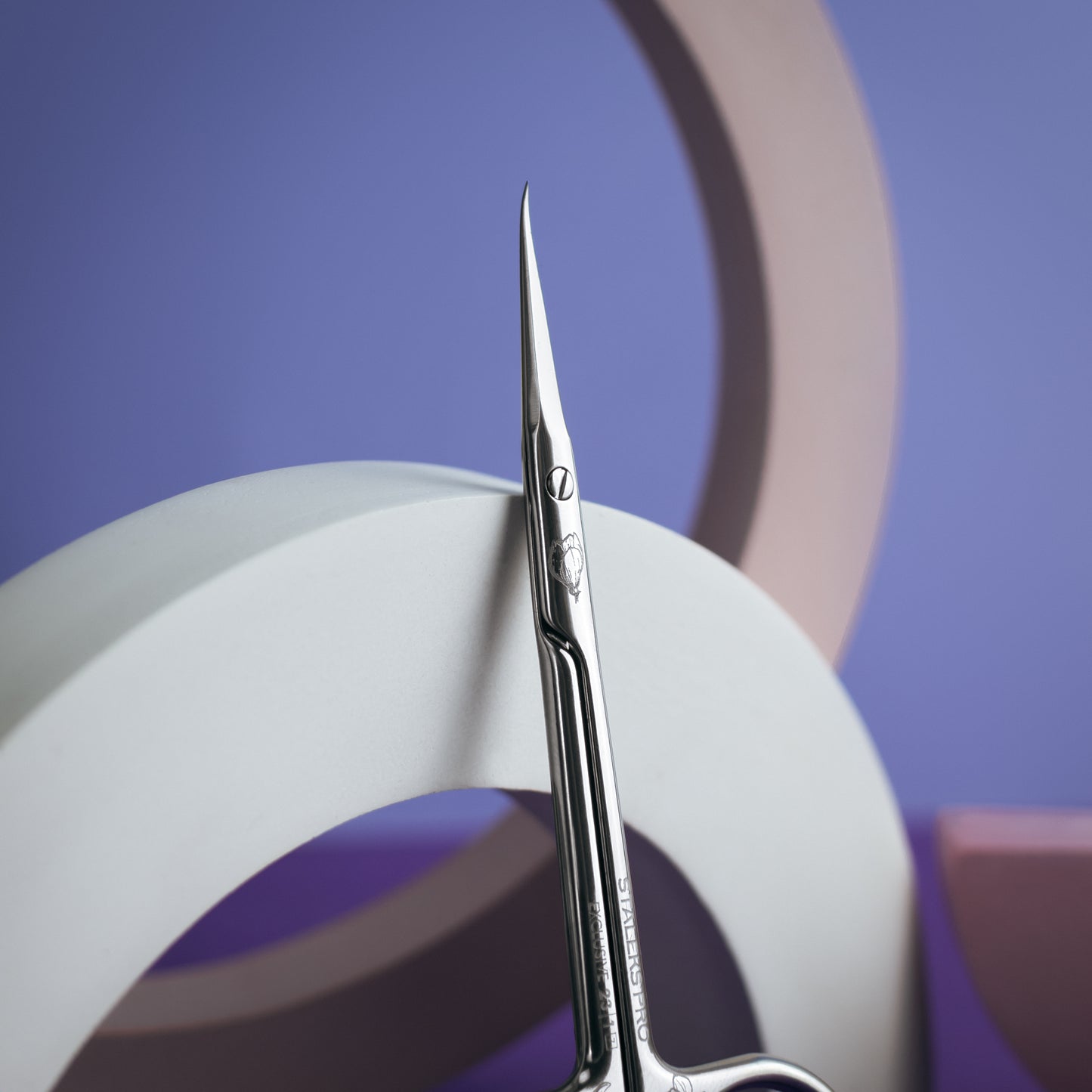 Sentence with product replaced: A pair of STALEKS PRO Professional cuticle scissors elongated handles (magnolia) EXCLUSIVE 23 TYPE 1 with surgically precise tips stands upright between abstract white paper curves, against a purple backdrop with a soft pink partial circle.