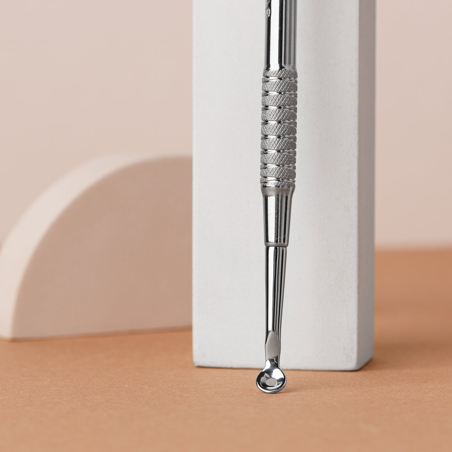 A close-up image of a Staleks STALEKS PRO Beauty care double-ended tool (UNO small and Vidal needle straight) EXPERT 21 TYPE 4 made of AISI 420 stainless steel, with a circular mirror at the end, positioned against a white and beige geometric background.