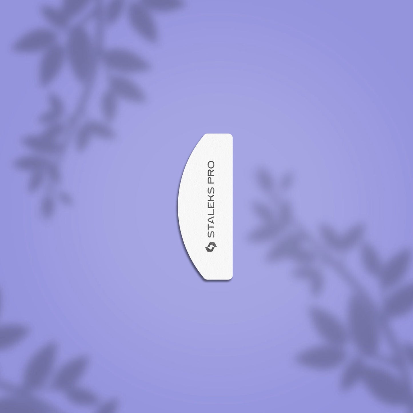 A white, curved Staleks PRO Grinding Buff Crescent mini EXPERT 41 100/180 grit nail file is centered on a light purple background with blurred leafy patterns, highlighting its abrasive coating for shaping artificial nails. (20 pcs).
