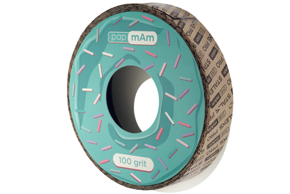 A roll of Staleks STALEKS PRO papMam White Disposable Abrasive Tape File EXPERT (Without Plastic Case) Atsc with a doughnut design, featuring pink and white sprinkles, marked as "100 grit". The roll is partially seen within a cardboard box.