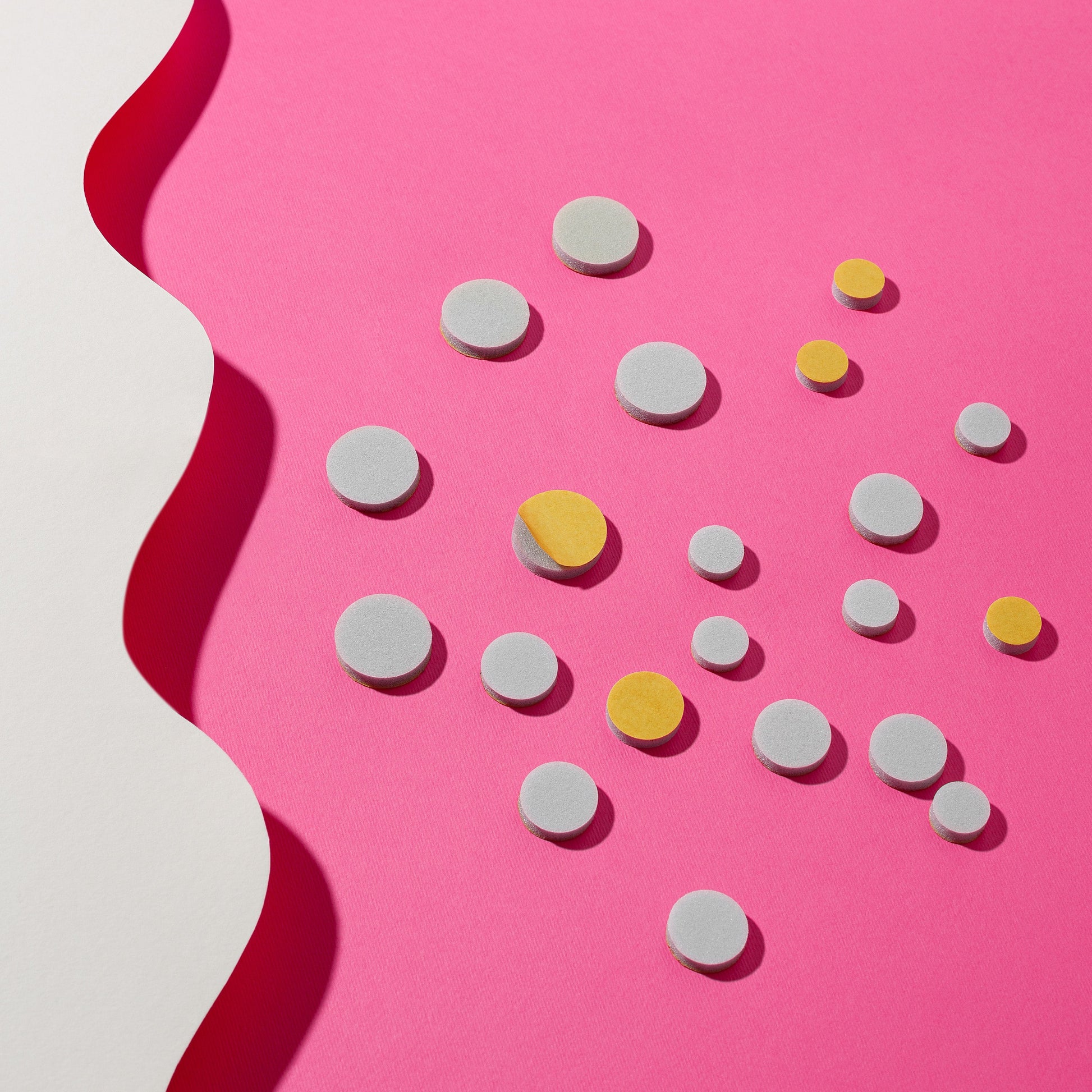 Staleks STALEKS PRO Disposable Files for Pedicure Disc PODODISC L EXPERT (25mm, 50pcs), gray and yellow, are arranged on a vivid pink background beside an uneven white border, forming a striking abstract visual.