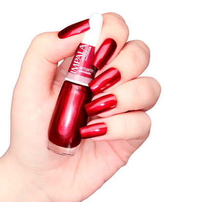 A hand with long, glossy red nails holds a bottle of Impala Regular Nail Polish Pearlescent Red Amante Perolado 7.5 ml against a white background.