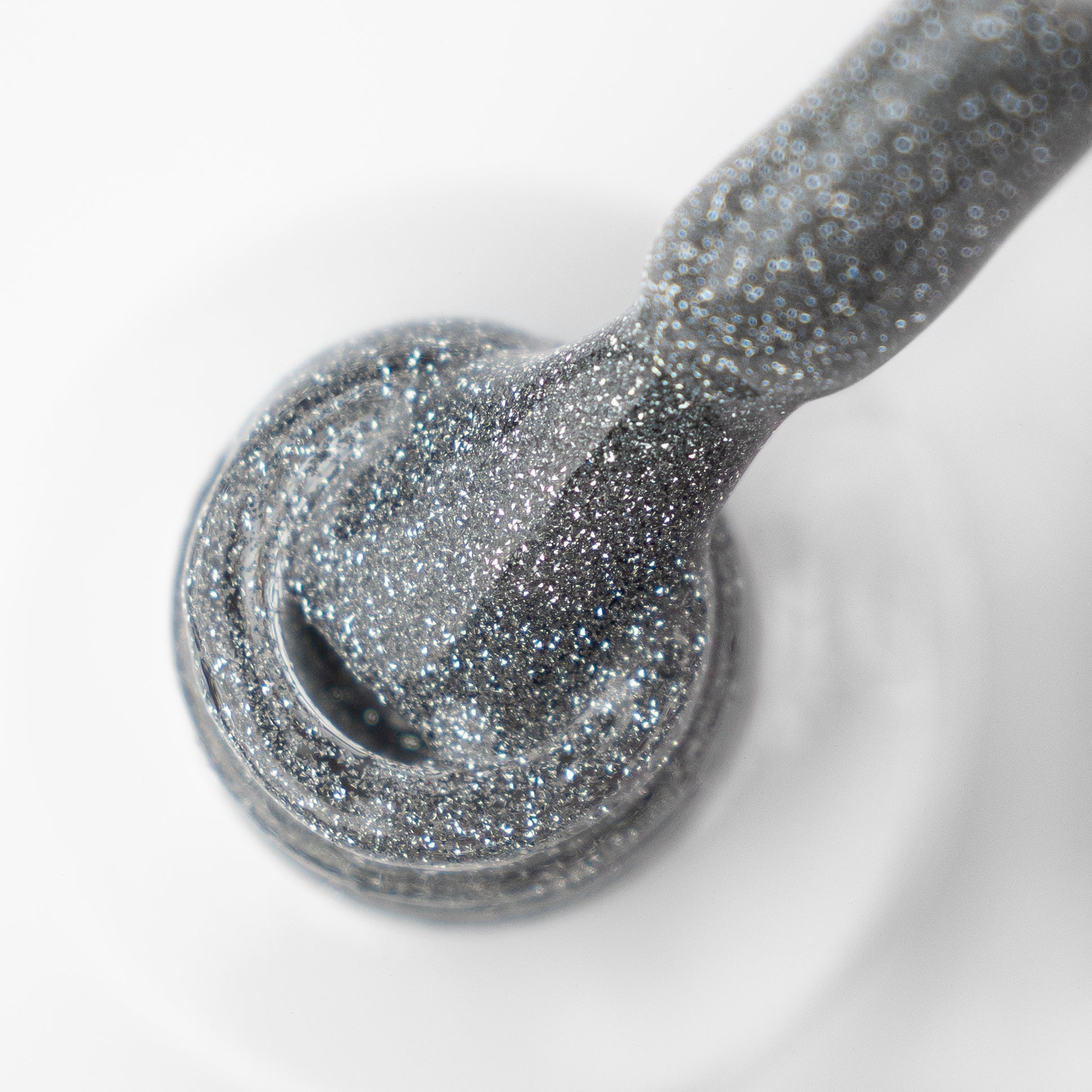 A close-up of a brush dipped into a bottle of LUMORE PARIS Reflective Gel Polish, Margarita (9 ml) by Lumore, showcasing its shimmery silver finish with fine glitter particles on both the brush and in the polish—ideal for crafting vibrant, eye-catching nail art designs.