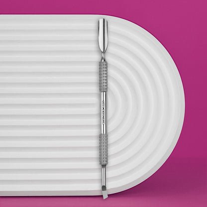 The Staleks PRO Manicure Pusher EXPERT 30 TYPE 4.2, featuring a rounded wide pusher and bent blade, rests on a white ridged surface with a bright pink background—ideal for precise cuticle work.