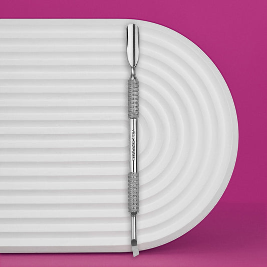 The Staleks PRO Manicure Pusher EXPERT 30 TYPE 4.2, featuring a rounded wide pusher and bent blade, rests on a white ridged surface with a bright pink background—ideal for precise cuticle work.