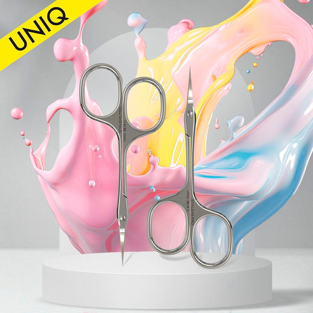 Two STALEKS PRO Professional Cuticle Scissors Asymmetric UNIQ 30 TYPE 4 by Staleks stand upright on a white round platform, set against pastel paint splashes with a yellow "UNIQ" label in the top left corner.