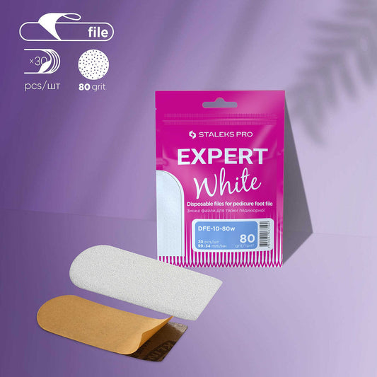 A pink Staleks "STALEKS PRO Refill Pads for Pedicure Foot File Expert 10" set shows three white disposable strips with brown adhesive, displayed on a lavender surface with a leaf shadow.