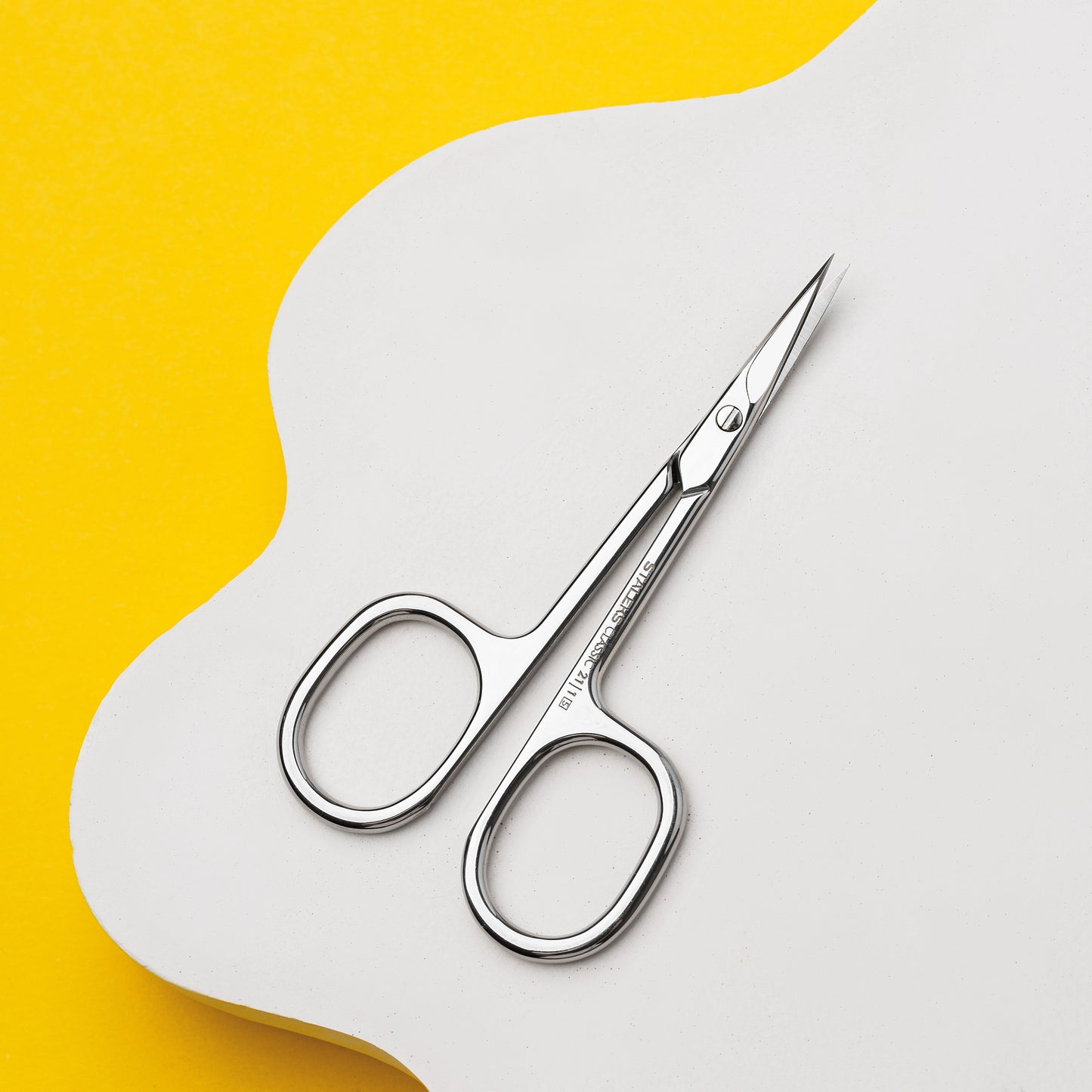 The STALEKS PRO Cuticle Scissors CLASSIC 21 TYPE 1 by Staleks, featuring stainless steel and rounded handles, rest on a white surface against a bright yellow background—an ideal tool for manicures and pedicures.