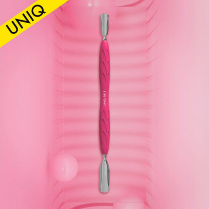 A pink dual-ended STALEKS PRO Gummy Manicure pusher with a silicone handle, featuring both wide and narrow rounded pushers, is displayed vertically on a textured pink background. In the top left, a yellow corner flag reads "UNIQ." Two soft pink round objects in the background enhance its appeal.