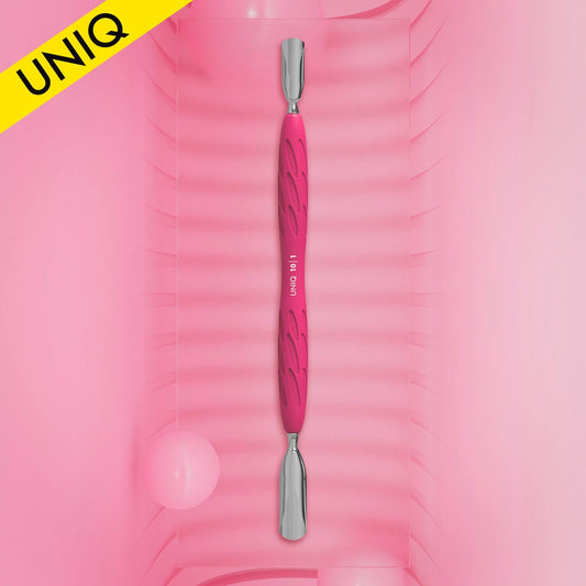 A pink dual-ended STALEKS PRO Gummy Manicure pusher with a silicone handle, featuring both wide and narrow rounded pushers, is displayed vertically on a textured pink background. In the top left, a yellow corner flag reads "UNIQ." Two soft pink round objects in the background enhance its appeal.