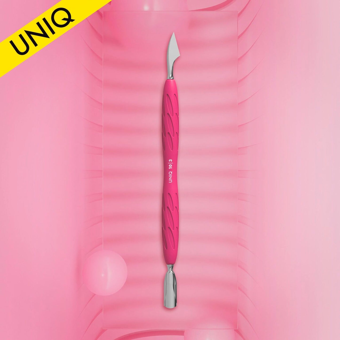 The STALEKS PRO Gummy Manicure Pusher with Silicone Handle UNIQ 10 TYPE 3, featuring a pink and silver design, is centered on a pink, ridged background. A yellow corner label displays "UNIQ." Two pink spheres in the background add to the soft, stylized appearance, ideal for manicure and pedicure sessions.