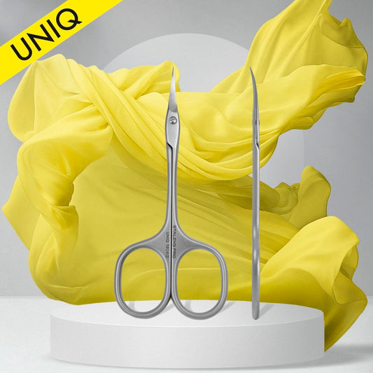 The STALEKS PRO Ballerina Professional Cuticle Scissors UNIQ 10 TYPE 4, by Staleks, is showcased in front and side views on a white platform against a backdrop of swirling yellow fabric. A yellow "UNIQ" label adorns the top left corner, highlighting the elegance and quality of these precision manicure tools.