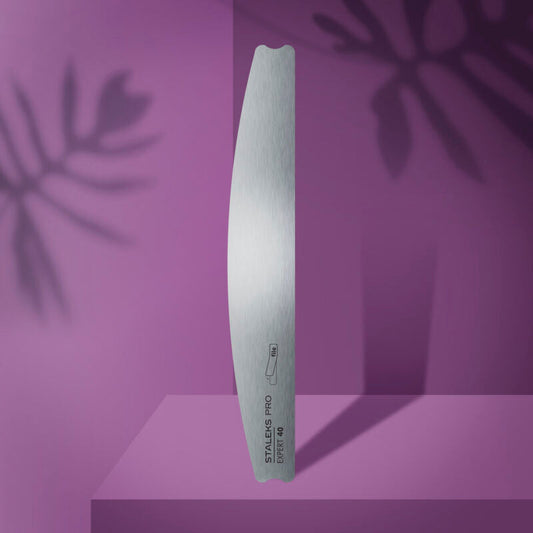 The STALEKS PRO Crescent Metal Base For Nail File EXPERT 40 by Staleks stands upright on a purple surface, with abstract leaf shadows in the background—showcasing the elegance and durability of this premium metal nail file.