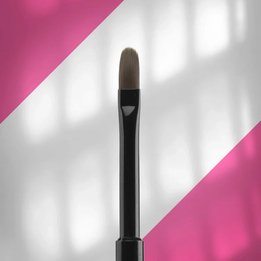 A close-up of the Staleks STALEKS PRO Brush for gel EXPERT (6 mm width, 11 mm length) with an oval shape, black handle, and flat synthetic bristles, positioned vertically against a pink and white diagonal background.