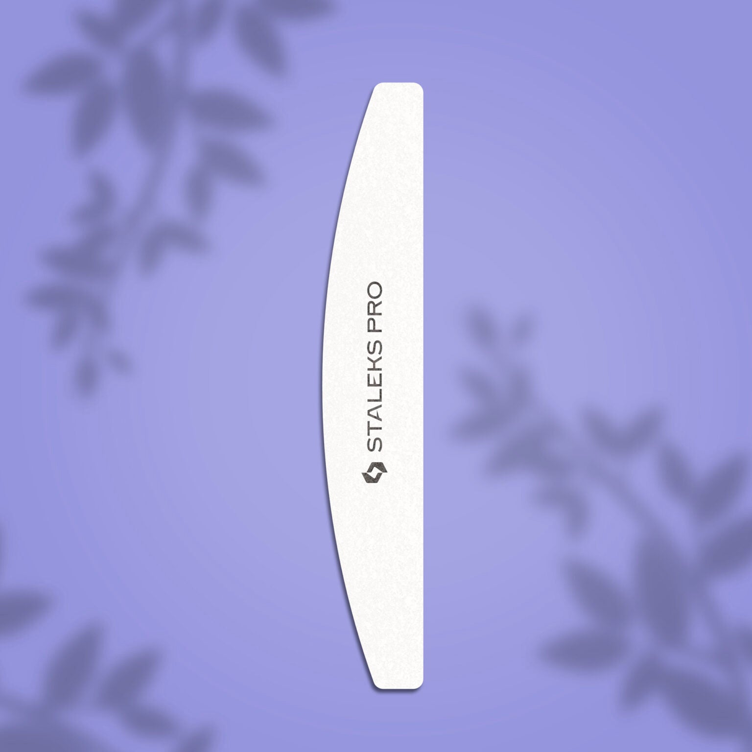 A white STALEKS PRO Grinding Buff crescent EXPERT 41 100/180 grit nail file (Staleks) lies vertically on a purple background with blurred leaf silhouettes, highlighting its fine abrasive surface.