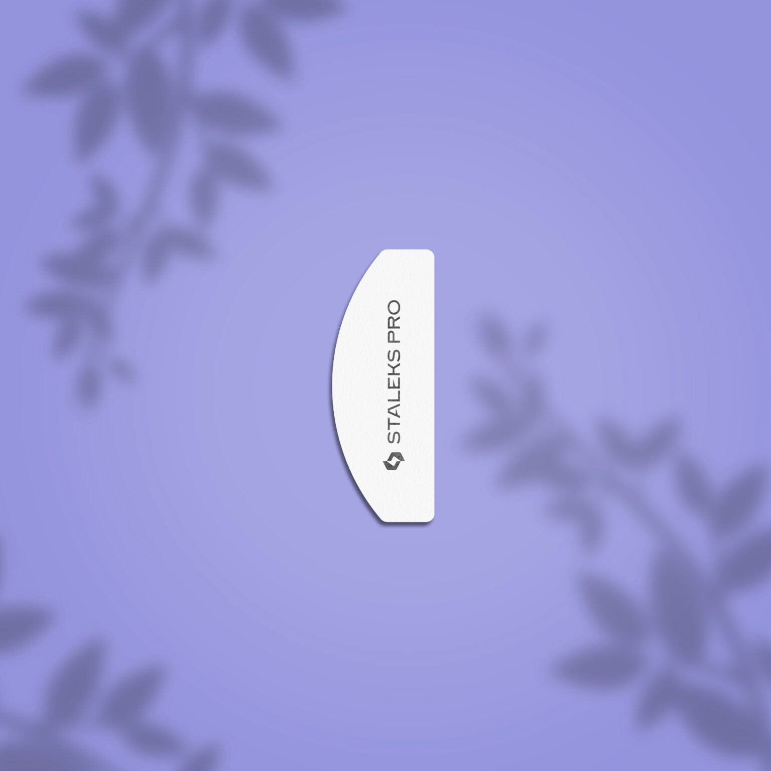 A white, curved Staleks PRO Grinding Buff Crescent mini EXPERT 41 100/180 grit nail file is centered on a light purple background with blurred leafy patterns, highlighting its abrasive coating for shaping artificial nails. (20 pcs).