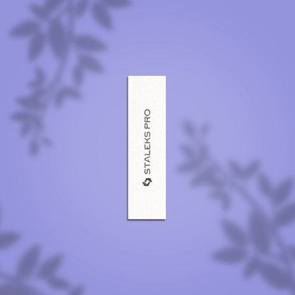 A white rectangular STALEKS PRO Grinding Buff EXPERT 51 150 grit nail file (10 pcs) with black vertical branding, displayed on a soft purple background with subtle blurred leaf shadows in the corners.