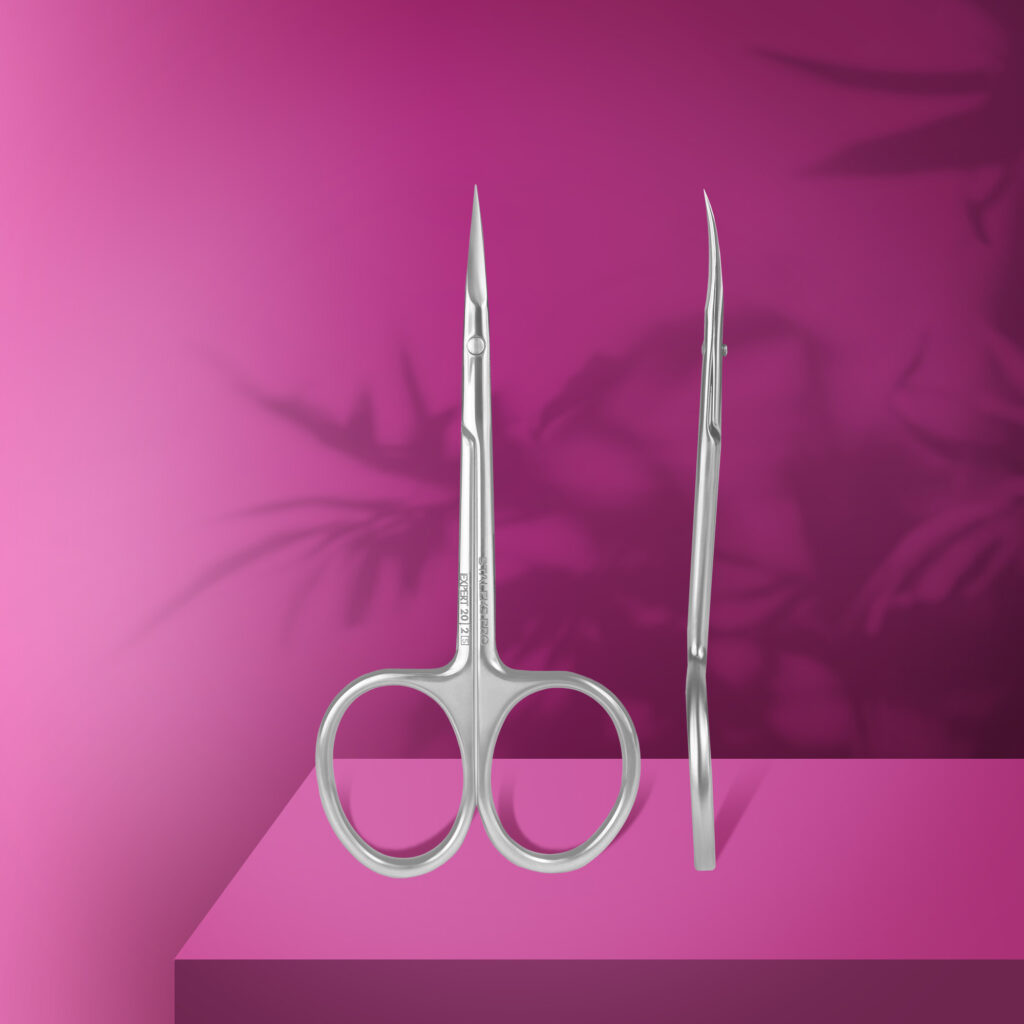 Staleks PRO Professional Cuticle Scissors EXPERT 20 TYPE 2 stand upright on a pink platform with soft leaf shadows in the background, showcasing their pointed high-alloy stainless steel blades.