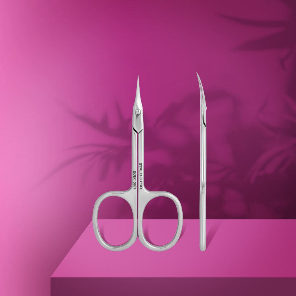 The STALEKS PRO Professional Cuticle Scissors EXPERT 50 TYPE 1 by Staleks, featuring pointed, curved stainless steel blades, stand upright on a bright pink surface with shadowy leaf patterns—ideal for any manicure routine.