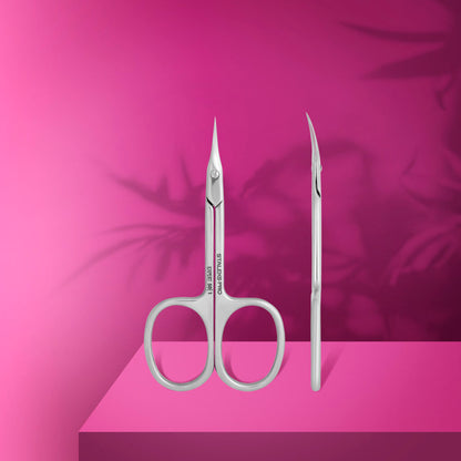 The STALEKS PRO Professional Cuticle Scissors EXPERT 50 TYPE 1 by Staleks, featuring pointed, curved stainless steel blades, stand upright on a bright pink surface with shadowy leaf patterns—ideal for any manicure routine.