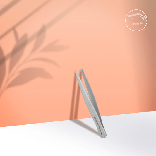 The STALEKS PRO Eyebrow Tweezers BEAUTY & CARE 10 TYPE 3 (wide beveled) by Staleks stands upright on a white surface with a peach background and leaf shadows. A white eye icon with bold brows and lashes appears in the top right corner.