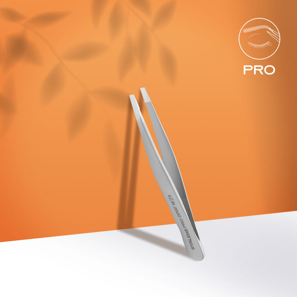 Staleks STALEKS PRO Eyebrow Tweezers EXPERT 10 TYPE 2 (narrow straight) in stainless steel stand upright on a white surface with an orange backdrop, leaf shadows, and a "PRO" eye logo—perfect for precise eyebrow correction.