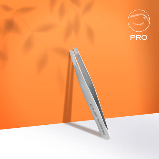 A pair of Staleks PRO Eyebrow Tweezers EXPERT 10 TYPE 3 (wide beveled), made of stainless steel, stands upright on a white surface with leaf shadows and an orange backdrop. The stylized eye logo and "PRO" appear in the top right corner.