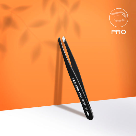 The STALEKS PRO Eyebrow Tweezers Black EXPERT 11 TYPE 4b (Narrow Beveled) by Staleks stand upright on an orange background with leaf shadows, ideal for eyebrow correction; a white eyelash logo appears in the top right corner.