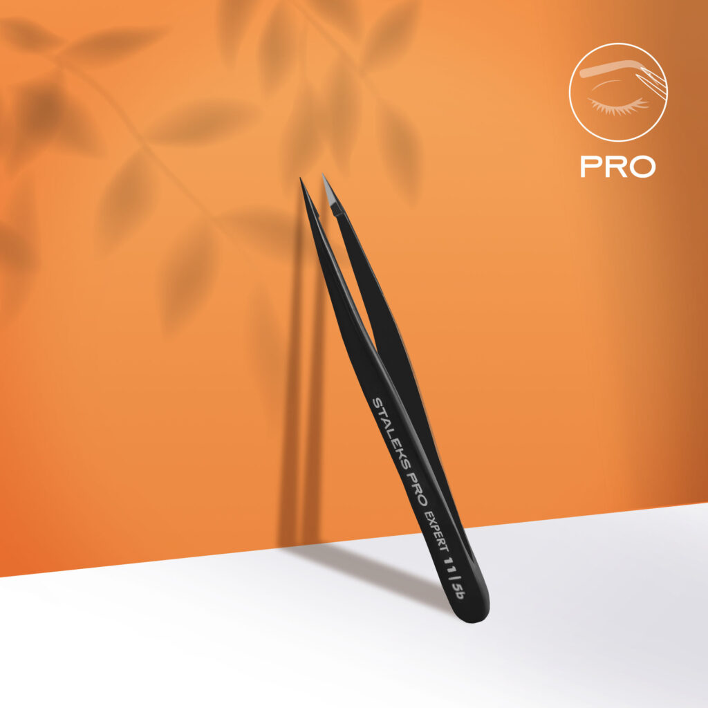 Staleks STALEKS PRO Eyebrow Tweezers Black EXPERT 11 TYPE 5b (point) stand upright against an orange background, ideal for eyebrow correction or ingrown hair removal, shown with a shadow and white surface below.