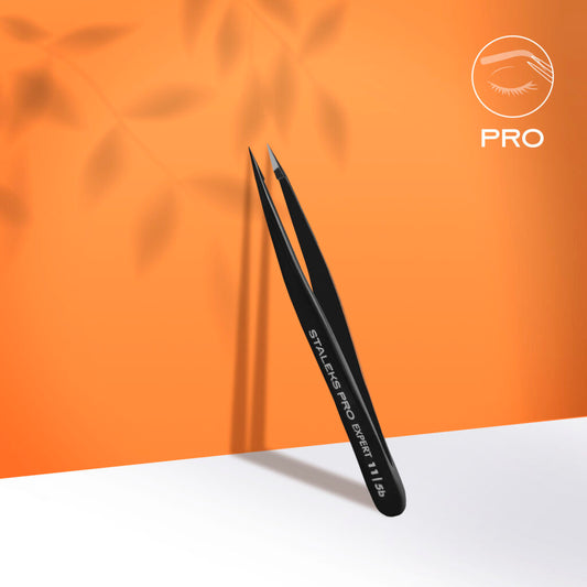 Staleks STALEKS PRO Eyebrow Tweezers Black EXPERT 11 TYPE 5b (point) stand upright against an orange background, ideal for eyebrow correction or ingrown hair removal, shown with a shadow and white surface below.