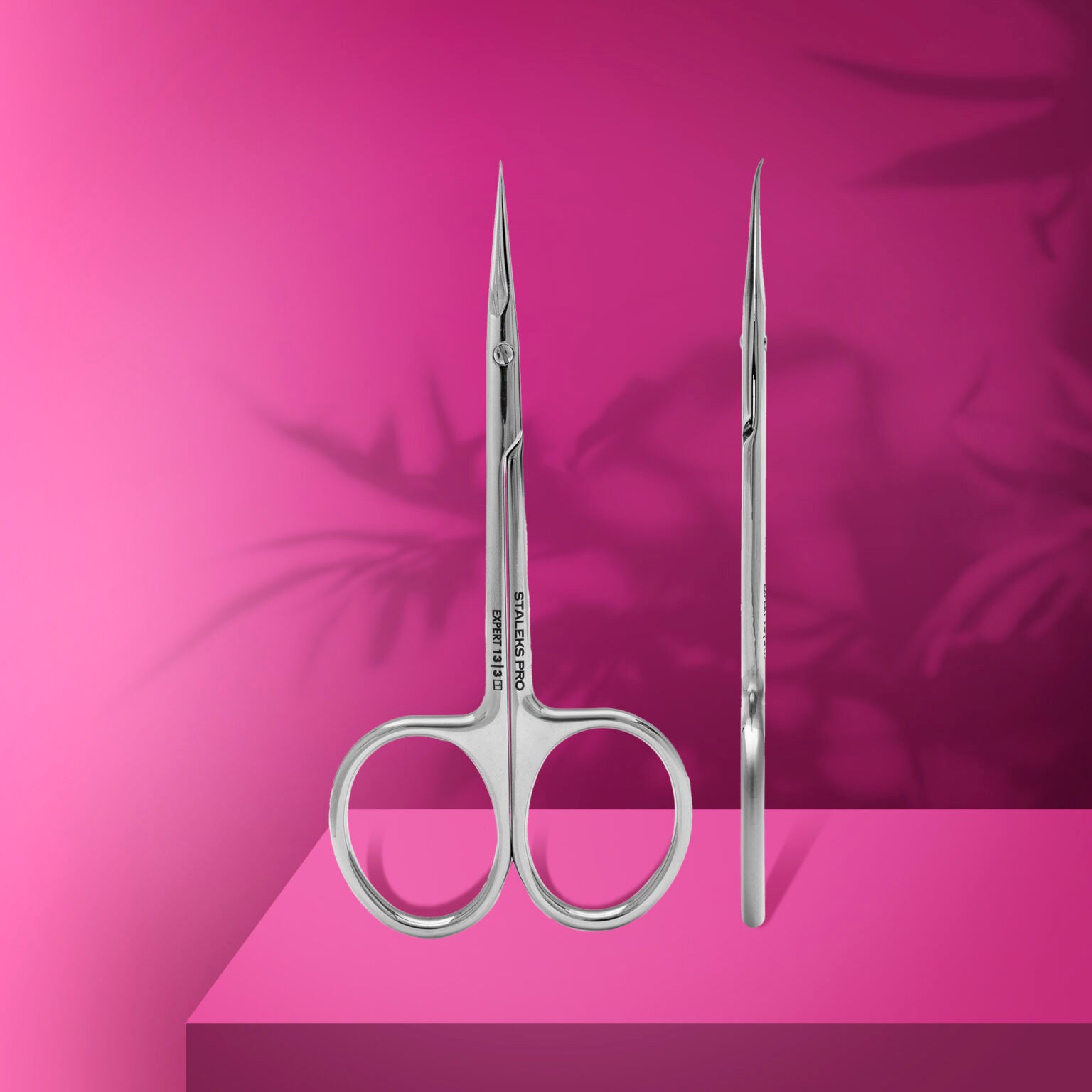 Two STALEKS PRO Professional Cuticle Scissors With Hook For Left-Handed Users EXPERT 13 TYPE 3 by Staleks are shown against a bright pink background, one forward and one side view, with soft leaf shadows in the back.