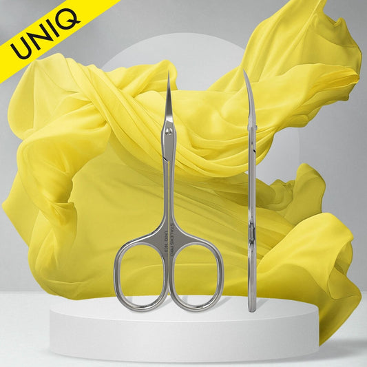 The Staleks STALEKS PRO Professional Cuticle Scissors Ballerina UNIQ 10 TYPE 3 are shown upright and sideways on a white platform, with a flowing yellow fabric backdrop and a "UNIQ" yellow banner in the top left corner.
