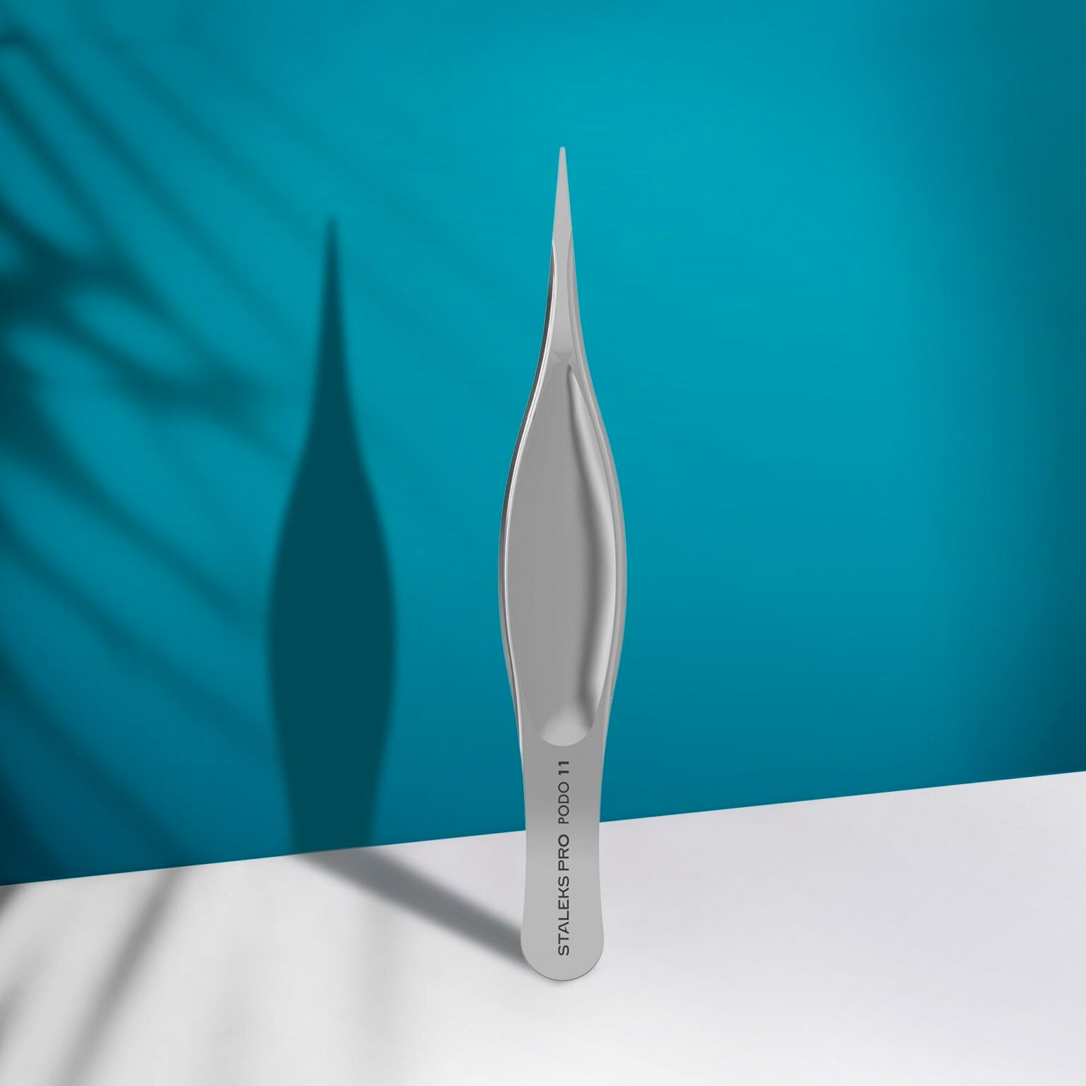 The STALEKS PRO Podology Splinter Tweezers Small PODO 11 by Staleks stands upright on a white surface under a teal background, ideal for ingrown nail care and recognized for its corrosion resistance.